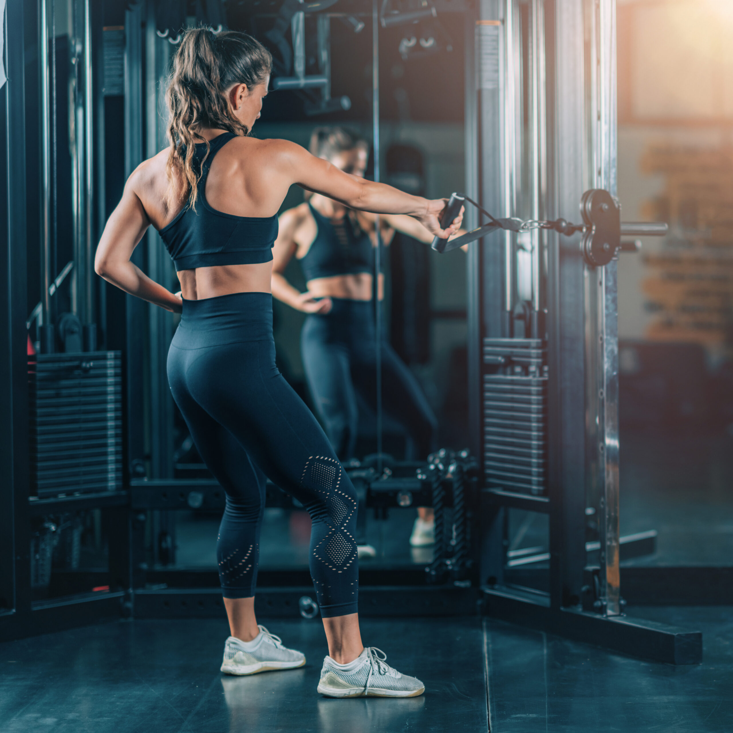 Spor salonunda kablolu fitness aletinde sırt antrenmanı yapan kadın